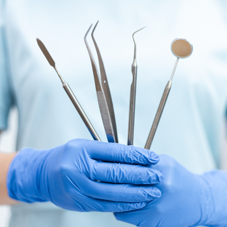 rankos su pirštinėmis laikančios odontologinius instrumentus